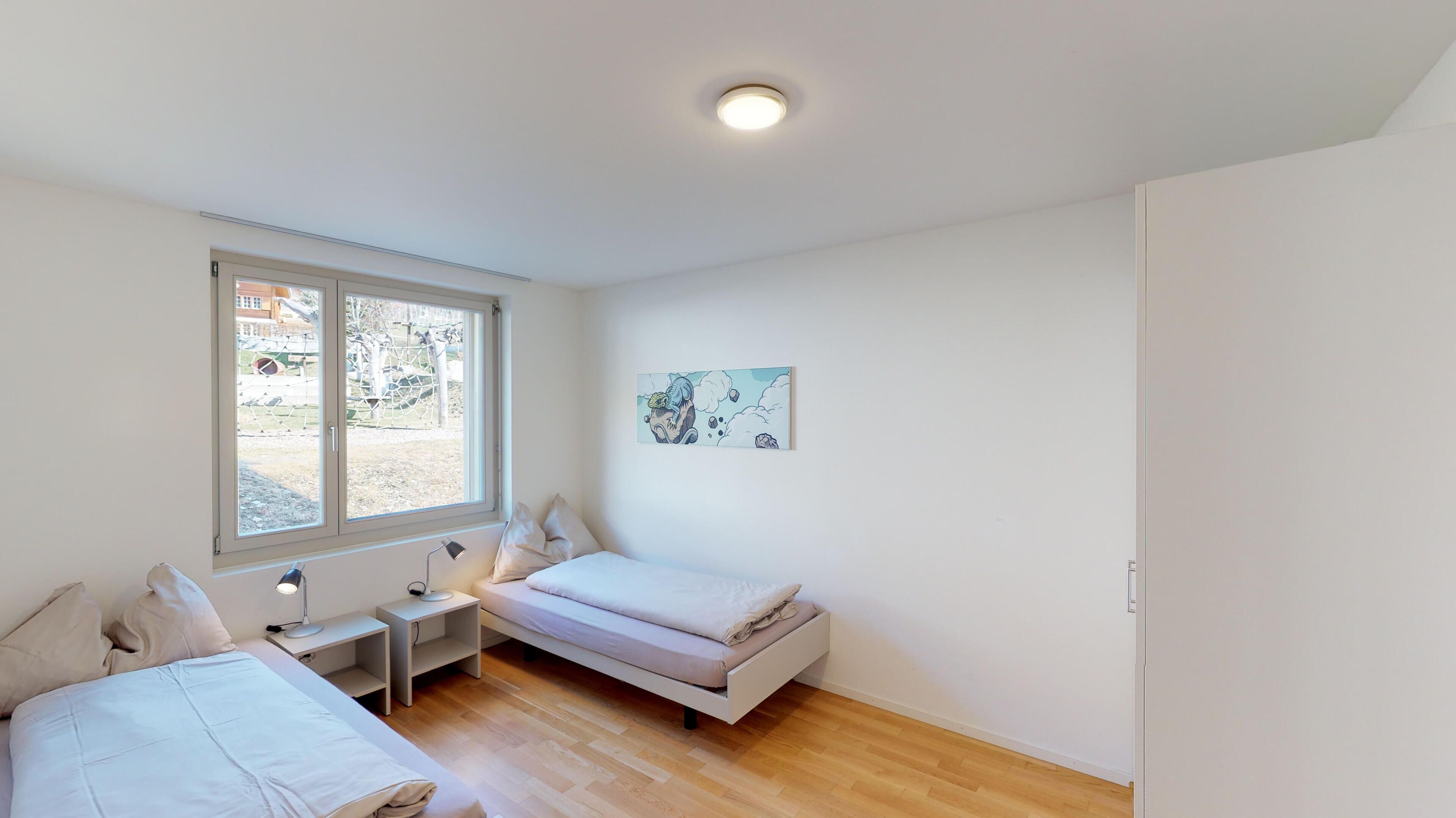 Un dormitorio con dos camas, una ventana, una mesita de noche con lámpara y una obra de arte en la pared.
