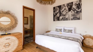 A bedroom with a bed, a mirror, a wall-mounted picture, and a door leading to a bathroom. - Spacious 3BR Villa W/ Garden & Pool in Bali, Bali Villa 2208 (Seminyak)