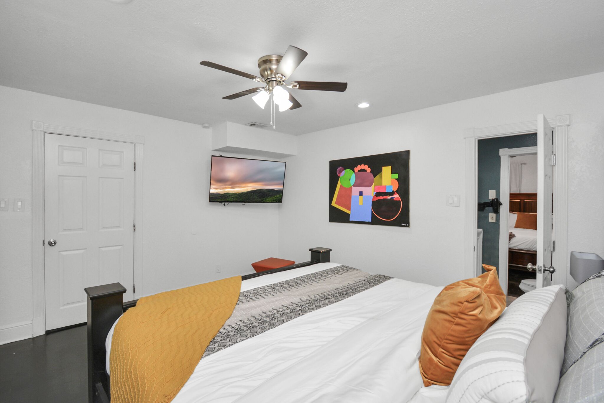 A bedroom with a bed, a ceiling fan, a painting, and a closet.