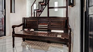 A wooden bench in a hallway with tiled flooring and a staircase in the background.