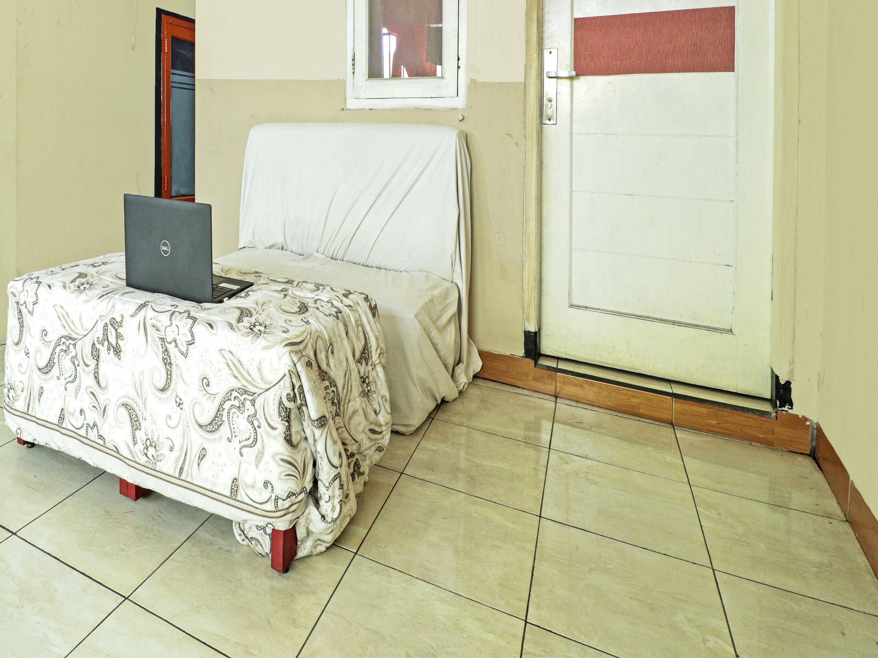 Una habitación con una cama, una computadora portátil sobre la cama, una puerta y una ventana.