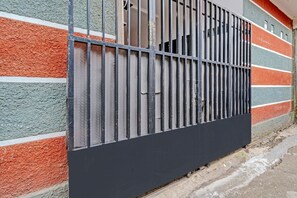 Una reja de metal negro con barras verticales, unida a un muro con rayas horizontales de colores.