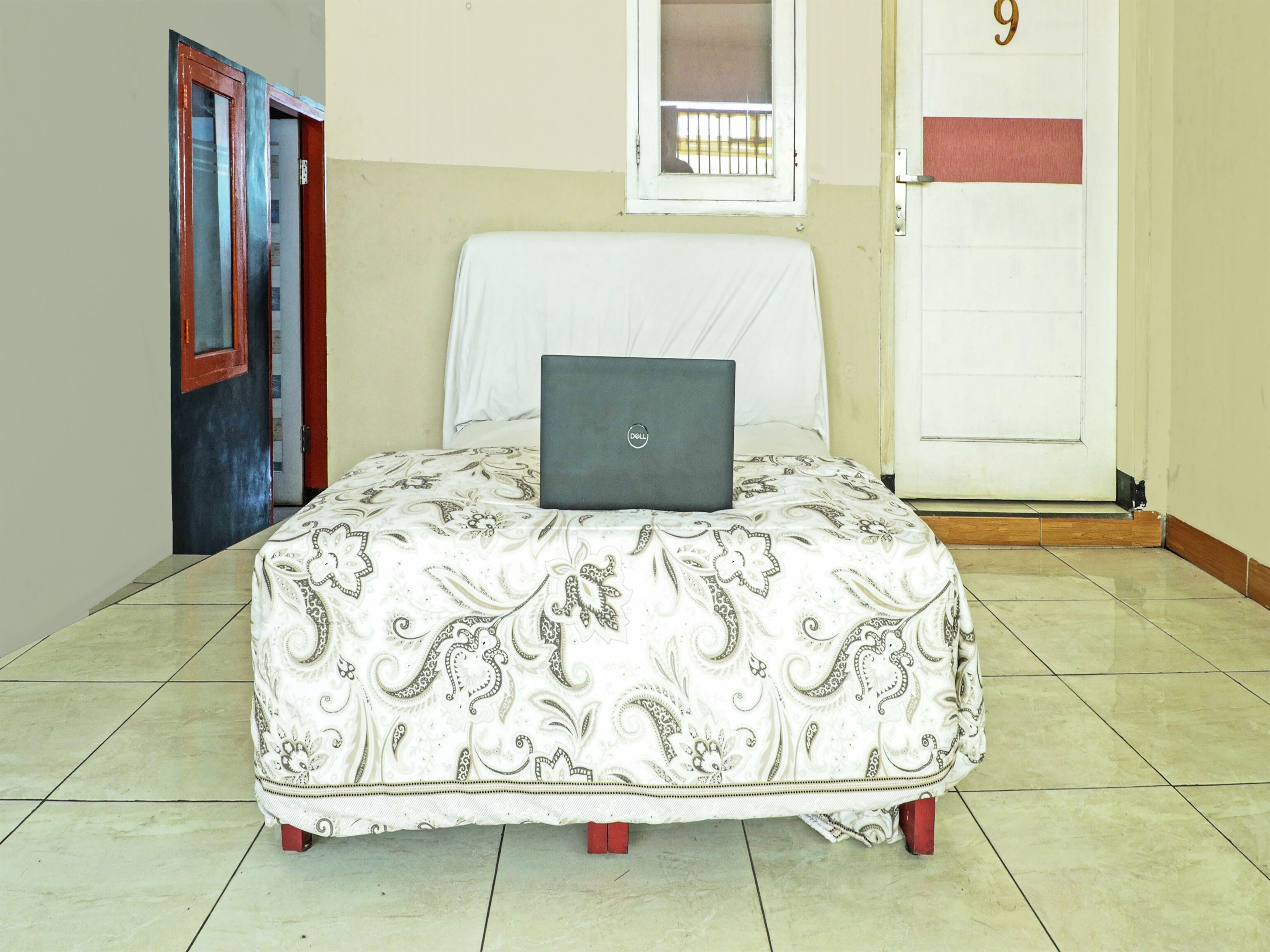 Un lit avec un ordinateur portable, une porte avec un numéro et une fenêtre.