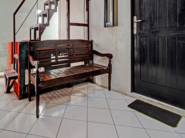 Un banco de madera con intrincados grabados, suelo de baldosas, una puerta negra y una escalera con barandilla de metal.