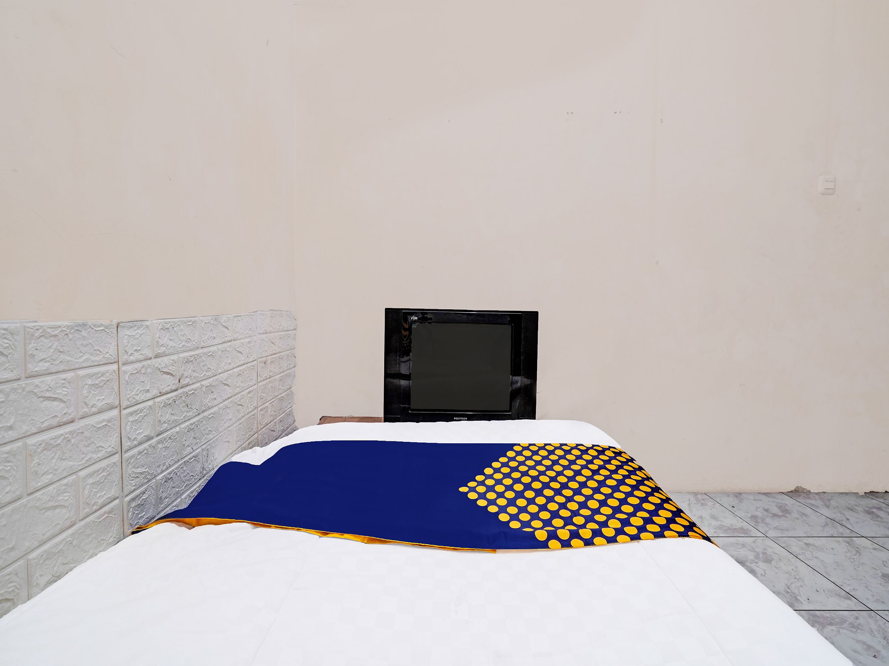 Ein Bett mit einer Decke in Blau und Gelb, einem weißen Kopfteil und einem schwarzen Fernseher an der Wand.