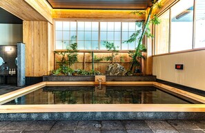 A traditional Japanese onsen with a wooden interior, a stone hot spring, and bamboo plants. - SPABLIC INN (Tokyo)
