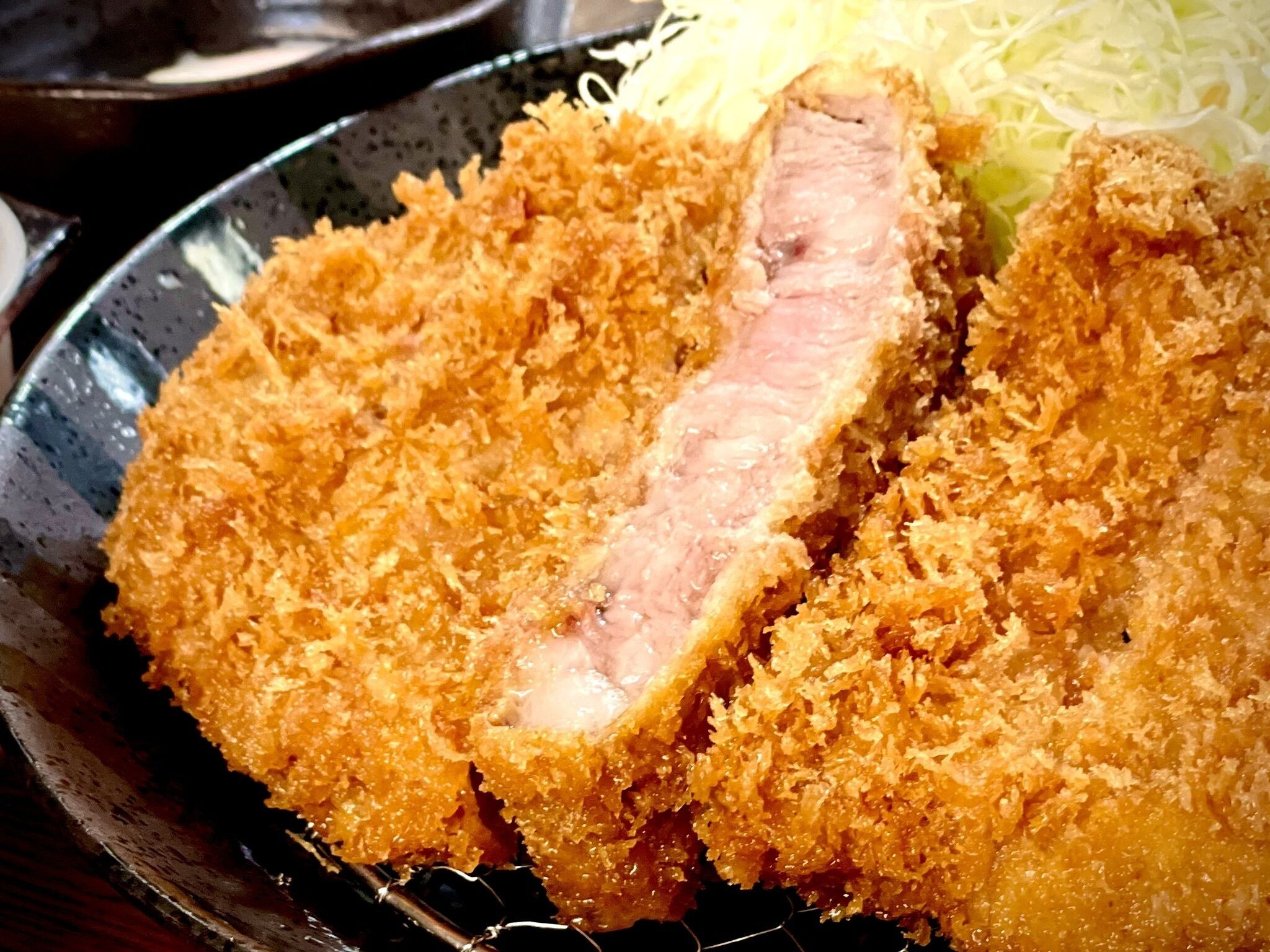 A close-up of a breaded and fried pork cutlet with a slice cut out, revealing the pink meat inside.