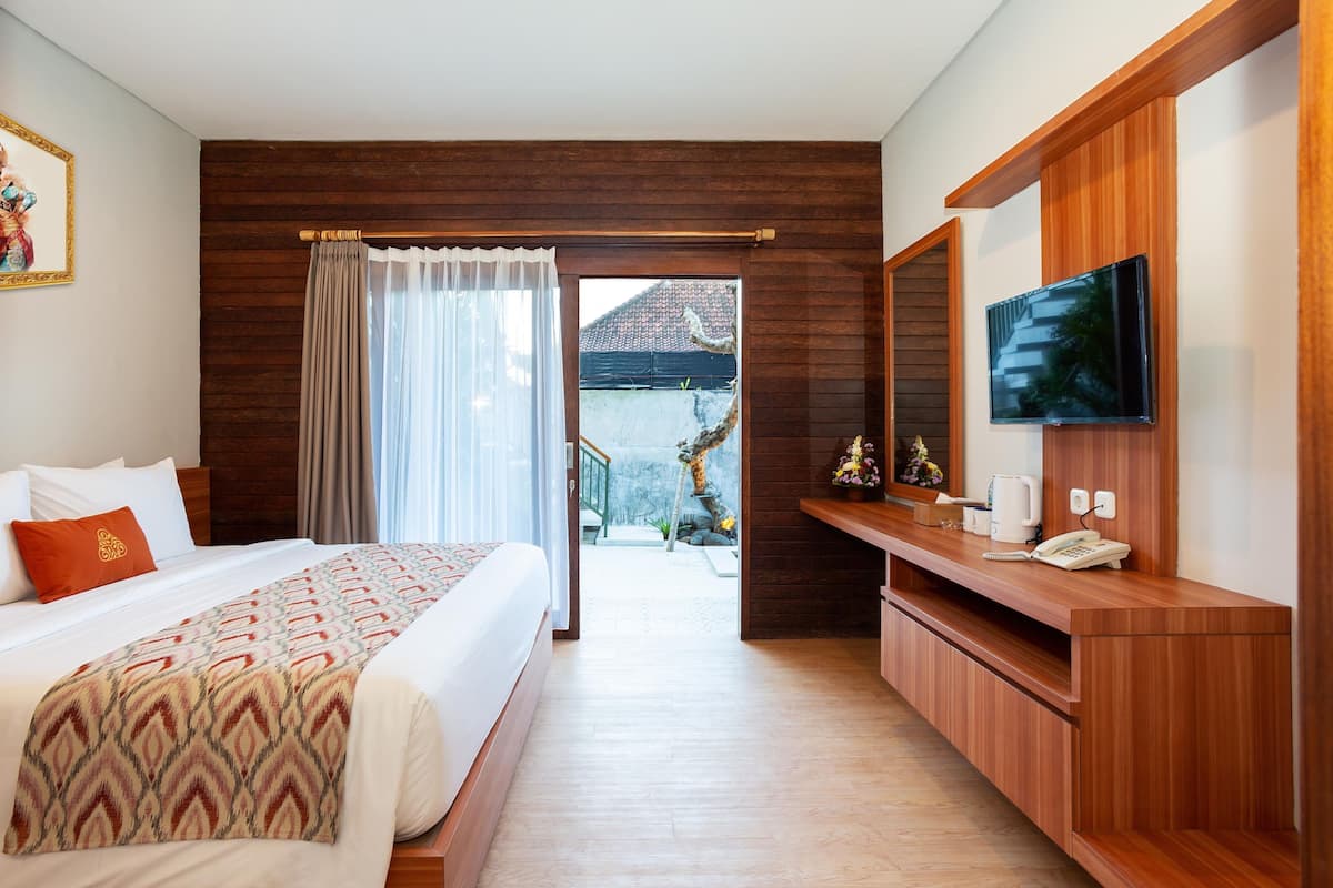 Habitación de hotel con cama, televisión, escritorio de madera y balcón con vistas.