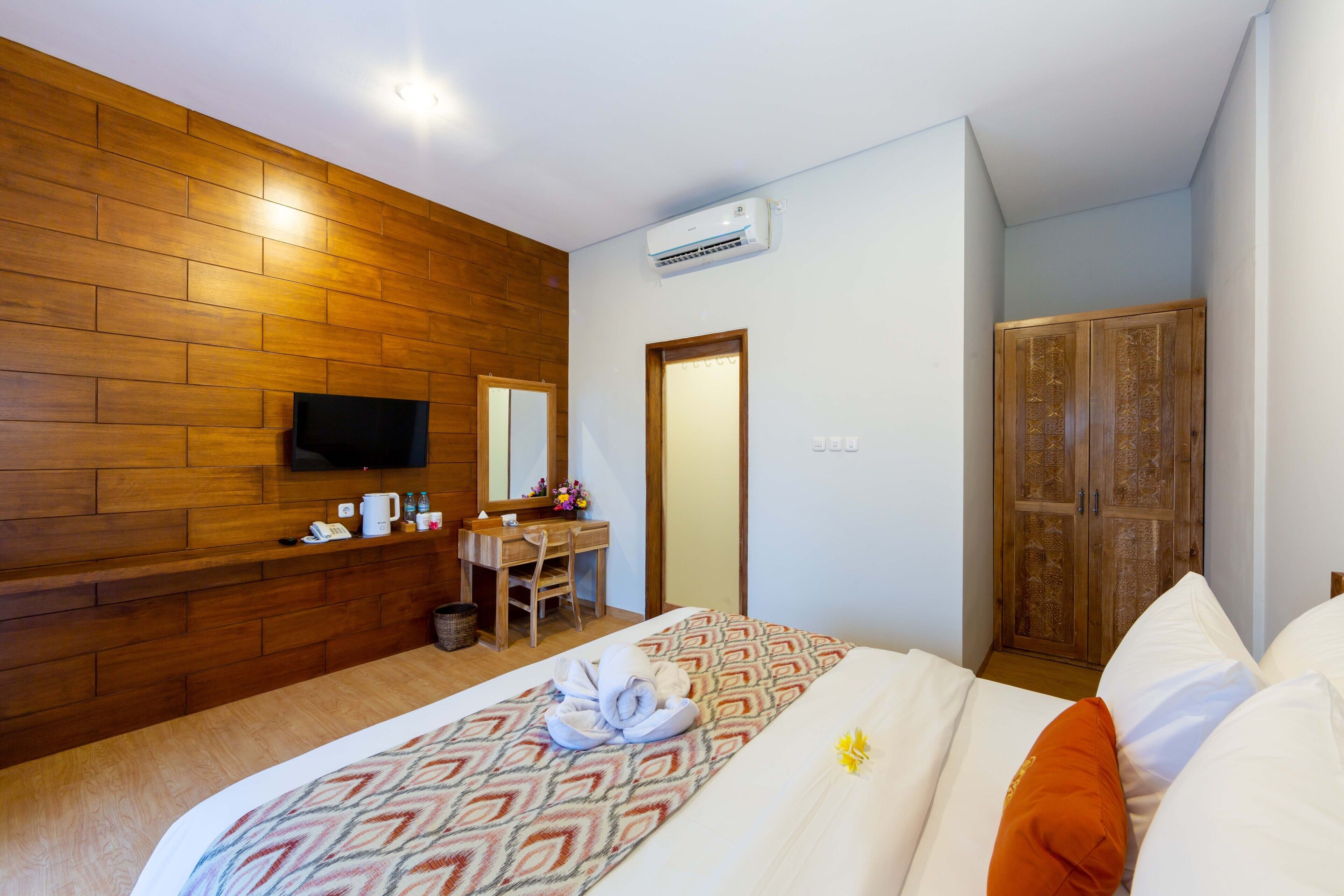 Hotellihuone, jossa on puinen seinä, kuviollinen vuodevaatteilla varustettu sänky, peilillä varustettu työpöytä ja vaatekaappi.