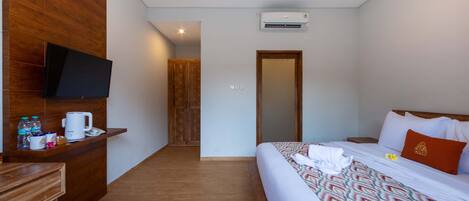 Una habitación de hotel con cama, televisor en la pared, escritorio de madera y cafetera.