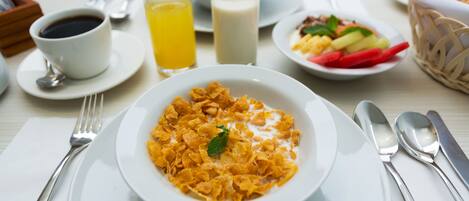 Un desayuno con cereal, leche, jugo de naranja y una taza de café sobre una mesa.