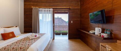 A hotel room with a bed, a TV mounted on the wall, a wooden floor, a balcony with a view, and a small table with a phone and toiletries.