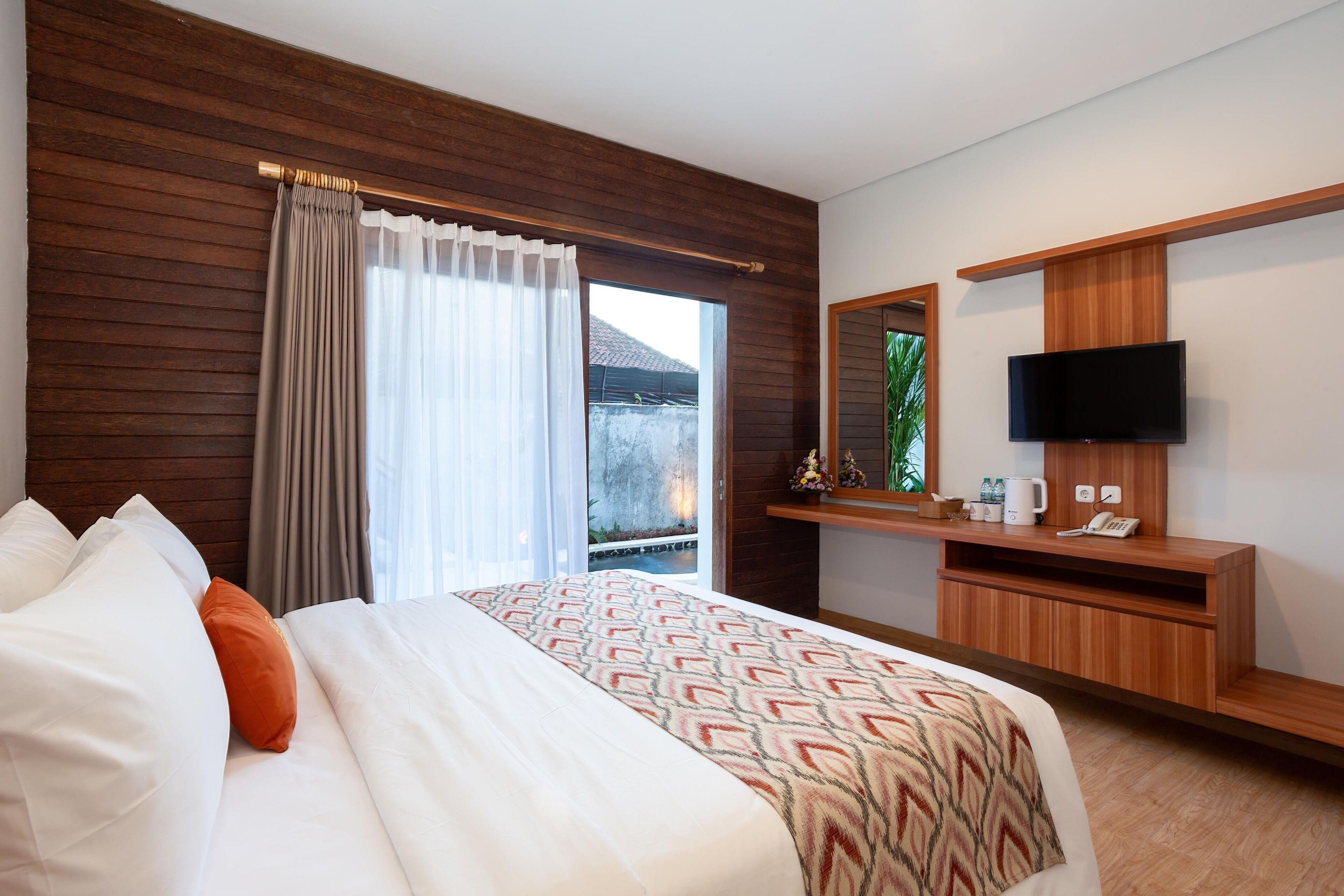 Een hotelkamer met een bed, een televisie, een houten bureau en een groot raam met gordijnen.