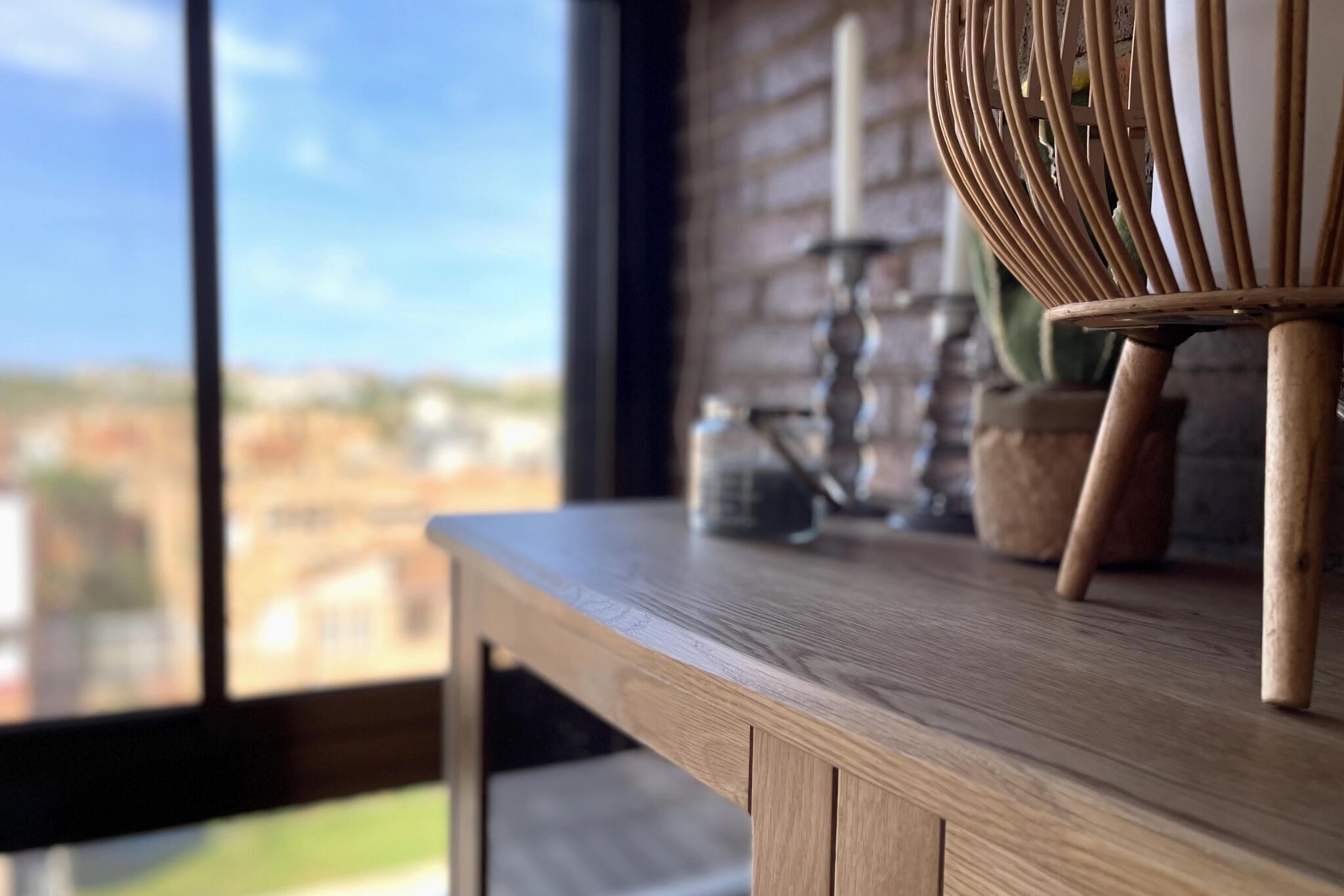 Ein Holztisch mit einem Korbstuhl, einem Kerzenhalter und einem Blumentopf.