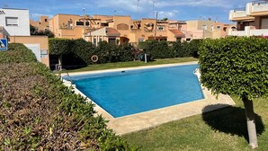 A swimming pool surrounded by well-maintained hedges and a residential area with multi-story buildings.