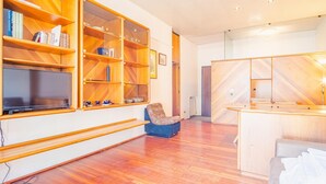 Uma sala de estar moderna com estantes de madeira, uma TV de tela plana, uma poltrona estampada e um armário de madeira.