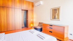 Quarto com cama, guarda-roupa de madeira, mesa de cabeceira, cadeira e um quadro na parede.