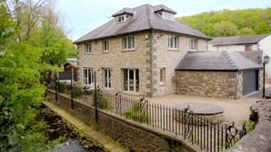 A stone house with a sloped roof, a small attached garage, and a paved courtyard.