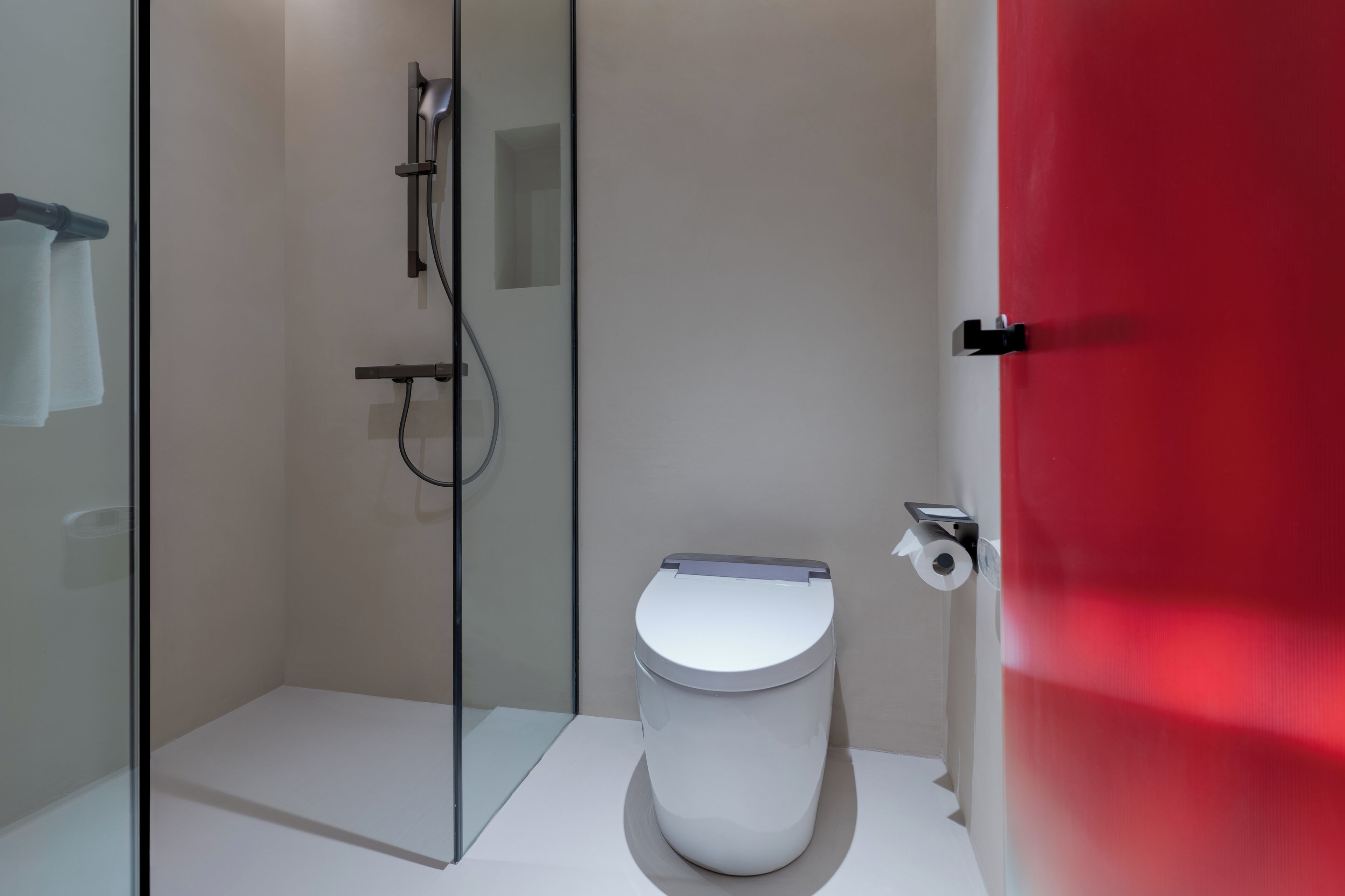 Un baño moderno con cabina de ducha de vidrio, inodoro blanco y puerta roja.