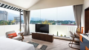 A modern hotel room with a large window, a flat-screen TV, a sofa, a desk, and a chair. - TELLUS. Qingchengshan Hot Spring Hotel (Chengdu)