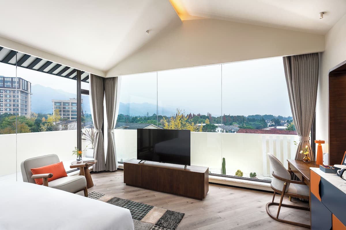 Une chambre d’hôtel moderne dotée d’une grande fenêtre, d’un téléviseur à écran plat, d’un canapé, d’un bureau et d’une chaise.