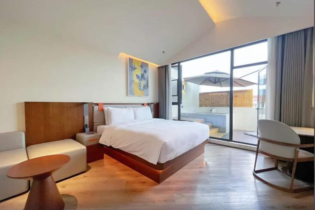 Une chambre d’hôtel moderne dotée d’un grand lit, d’un coin salon avec une table et d’une vue dégagée sur l’extérieur grâce à une porte vitrée.