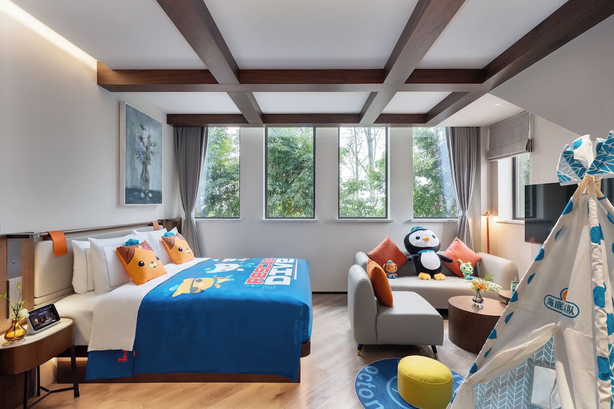 Une chambre d’hôtel avec un lit, un canapé, une structure ressemblant à une tente et une fenêtre donnant sur des arbres.