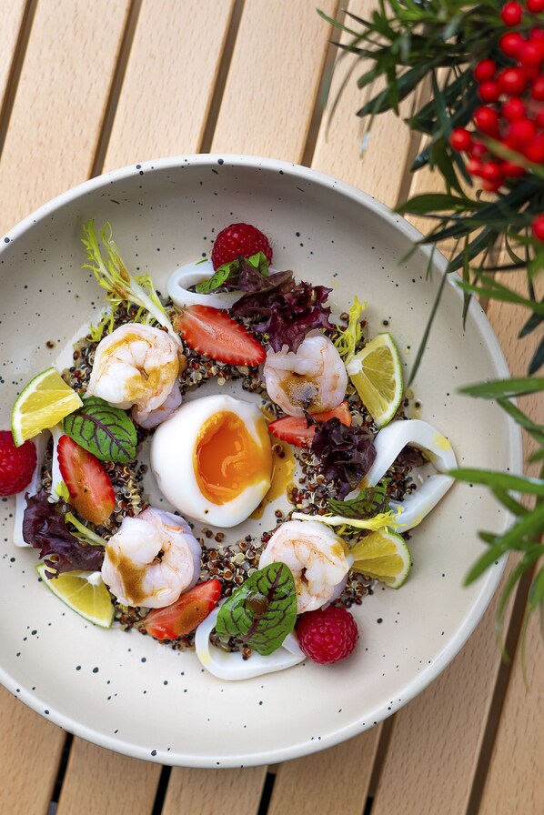 Un tazón de ensalada con camarones, fresas y un huevo cocido sobre una mesa de madera.