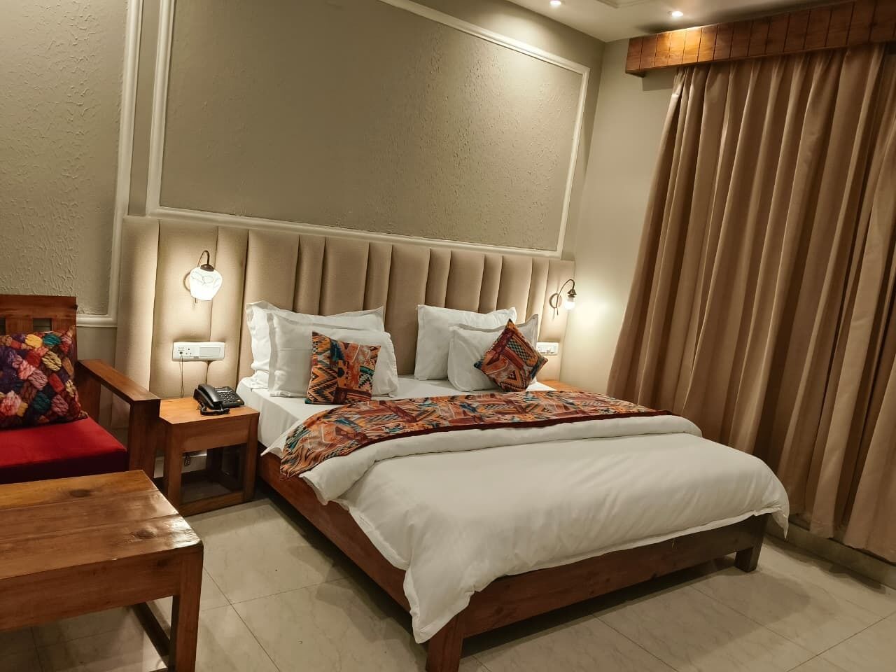A hotel room with a bed, bedside tables, a nightstand, a chair, and a window with curtains.