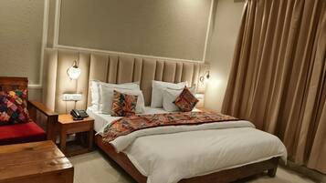 A hotel room with a bed, bedside tables, a nightstand, a chair, and a window with curtains.