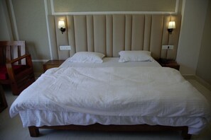 Ein ordentlich gemachtes Bett mit weißen Leinen, zwei Nachttischlampen und ein Nachttisch aus Holz mit einem Telefon.