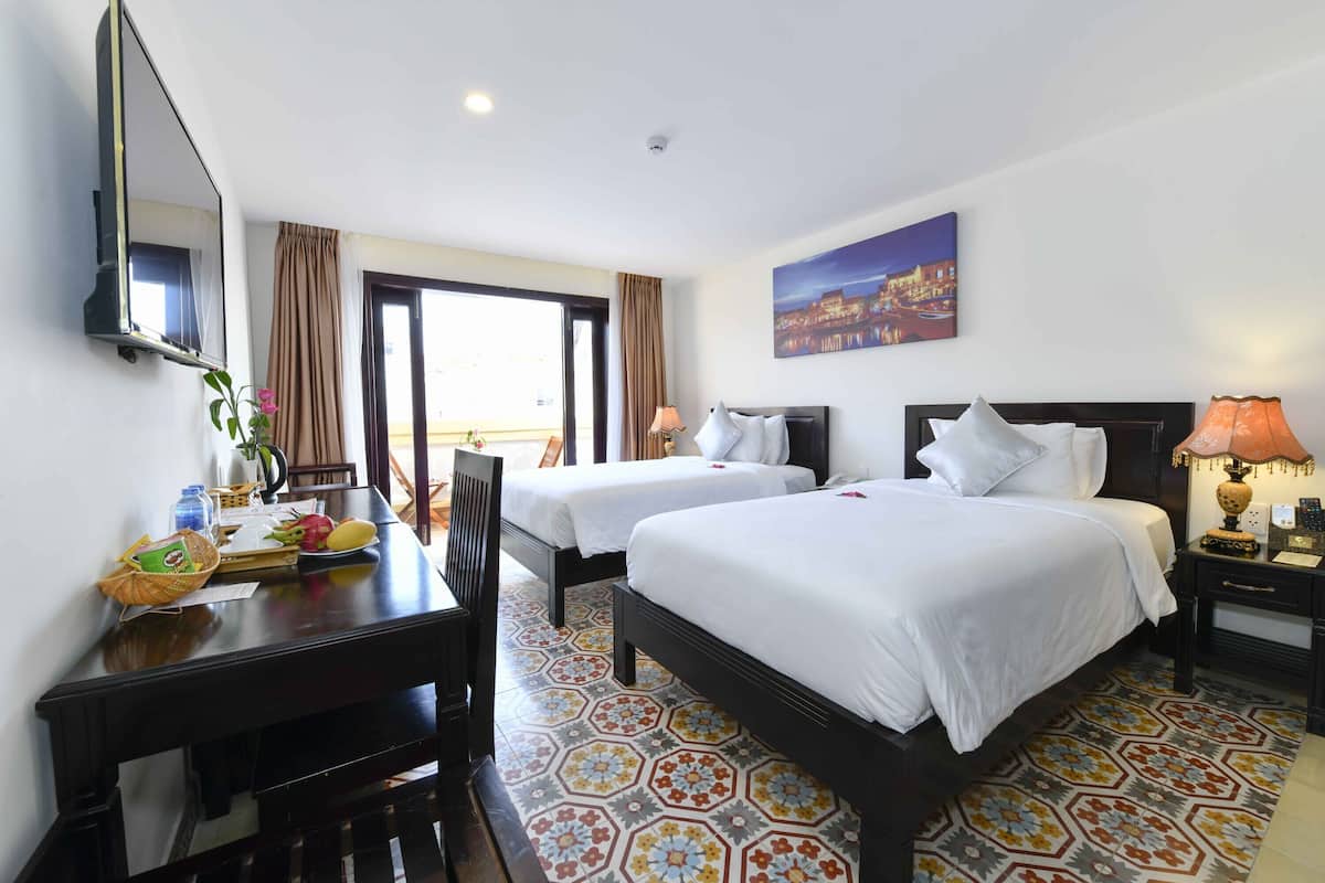Une chambre d’hôtel avec deux lits, un bureau, une chaise, une télévision et une fenêtre avec des rideaux.