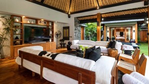 A spacious living area with a large flat-screen TV, comfortable seating, and a view of the outdoor garden. - Cheerful 3BR Villa W/ Pool & Garden, Bali Villa 2213 (Seminyak)