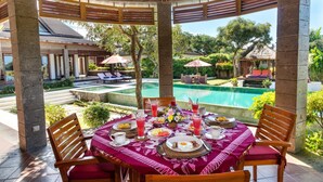 Un coin repas avec une table mise pour le petit-déjeuner, donnant sur une piscine et un jardin.