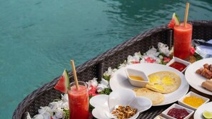A dining setup by a pool with a wicker table, plates of food, and drinks. - Airy 7BR Villa With Amazing Hot Tub & Pool, Bali Villa 2234 (Sukawati)