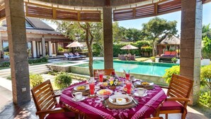 A covered outdoor dining area with a pool view, featuring a table set for breakfast with various dishes and drinks. - Airy 7BR Villa With Amazing Hot Tub & Pool, Bali Villa 2234 (Sukawati)