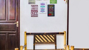 Une pièce avec une porte en bois, une table en verre et une chaise en bambou. Plusieurs panneaux sont accrochés au mur.