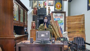Un bureau en bois, un ordinateur, une chaise et une pile de tapis tissés.