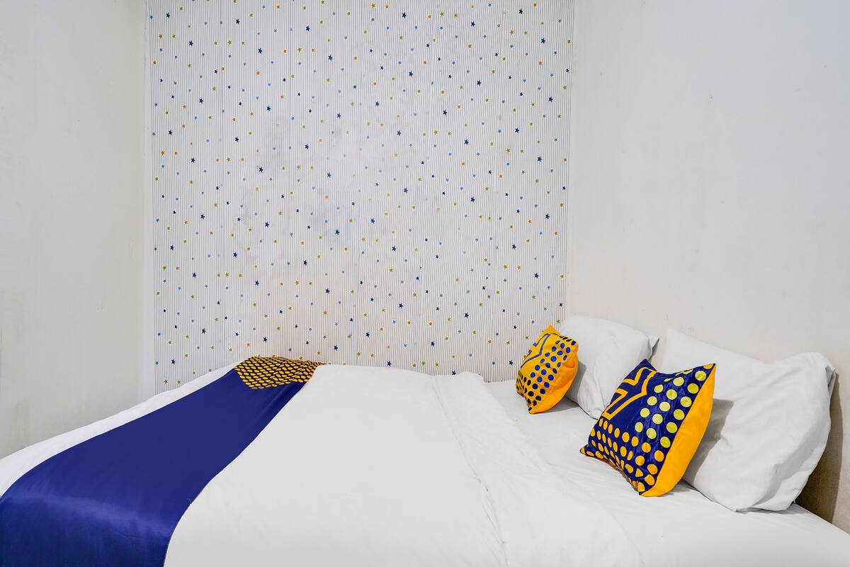 A neatly made bed with a blue and yellow bedspread, white pillows, and a polka-dotted pillow.