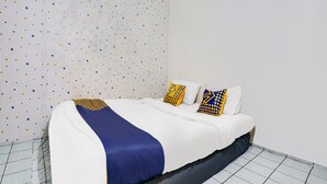 Un lit bien fait, recouvert d’une couvre-lit bleue et blanche, avec deux oreillers aux motifs géométriques et un rideau à rayures.