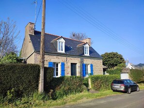 Une maison en pierre avec des volets bleus, une cheminée et une voiture garée.