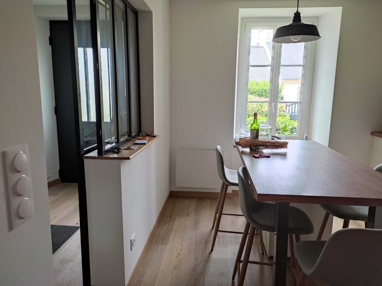 Ett modernt kök med en bänkskiva i trä, ett matbord med stolar, en hängande lampa och ett fönster med utsikt över grönområden.