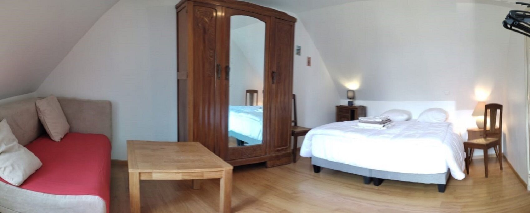 Un dormitorio con una cama, un armario de madera, una mesita, un sofá rojo y dos lámparas de noche.