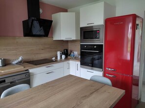 Une cuisine compacte avec une table en bois, des placards blancs, un réfrigérateur rouge et un four encastré.