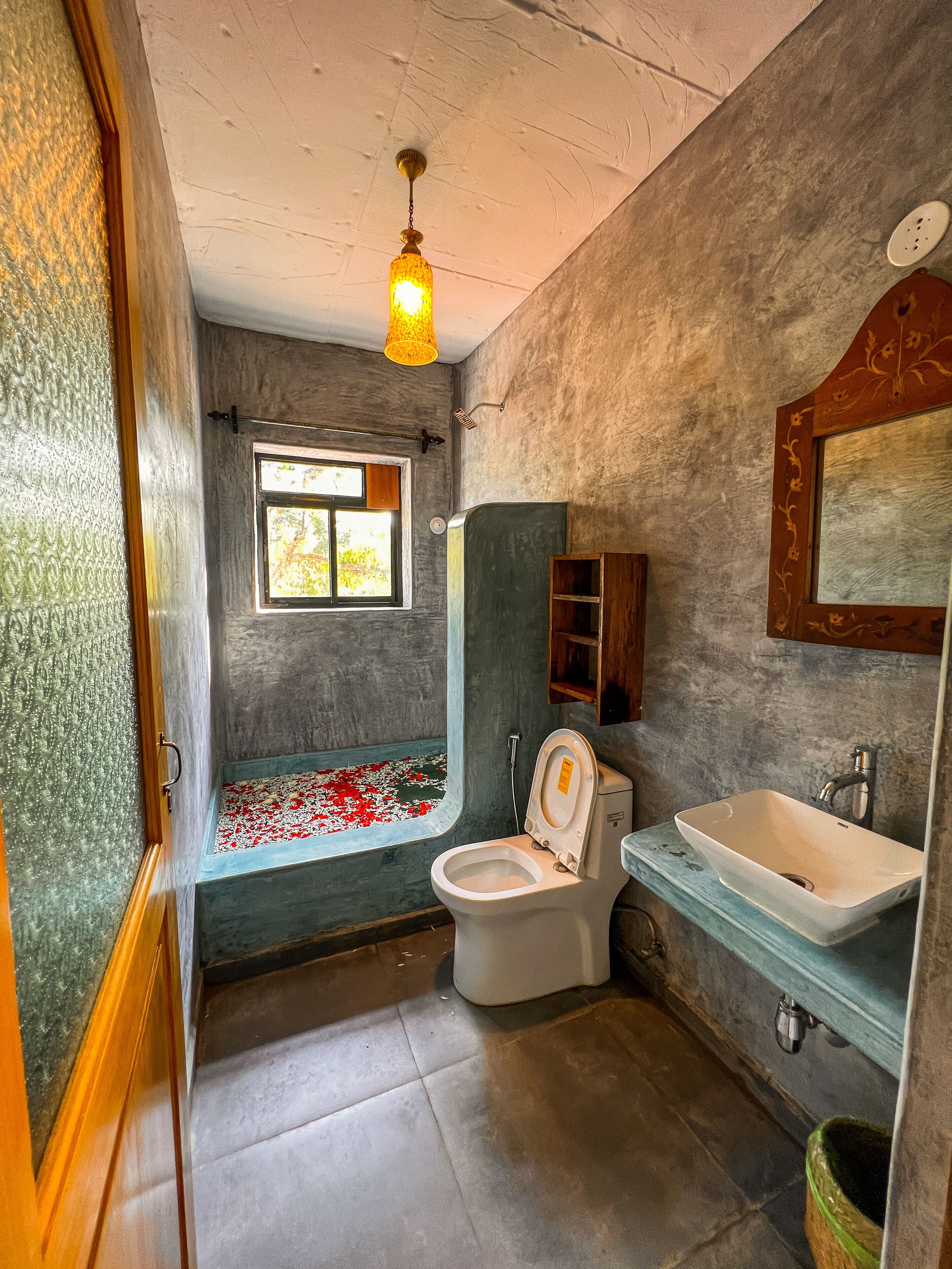 Un baño con bañera, inodoro, lavamanos y ventana con vista a árboles.