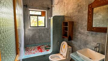 Un baño con bañera, inodoro, lavamanos y ventana con vista a árboles.