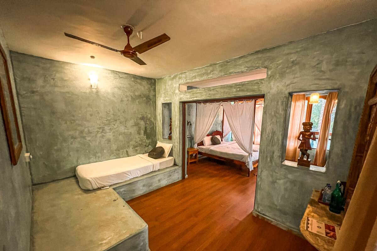 A room with a bed, a small bench, a ceiling fan, and a window with curtains.