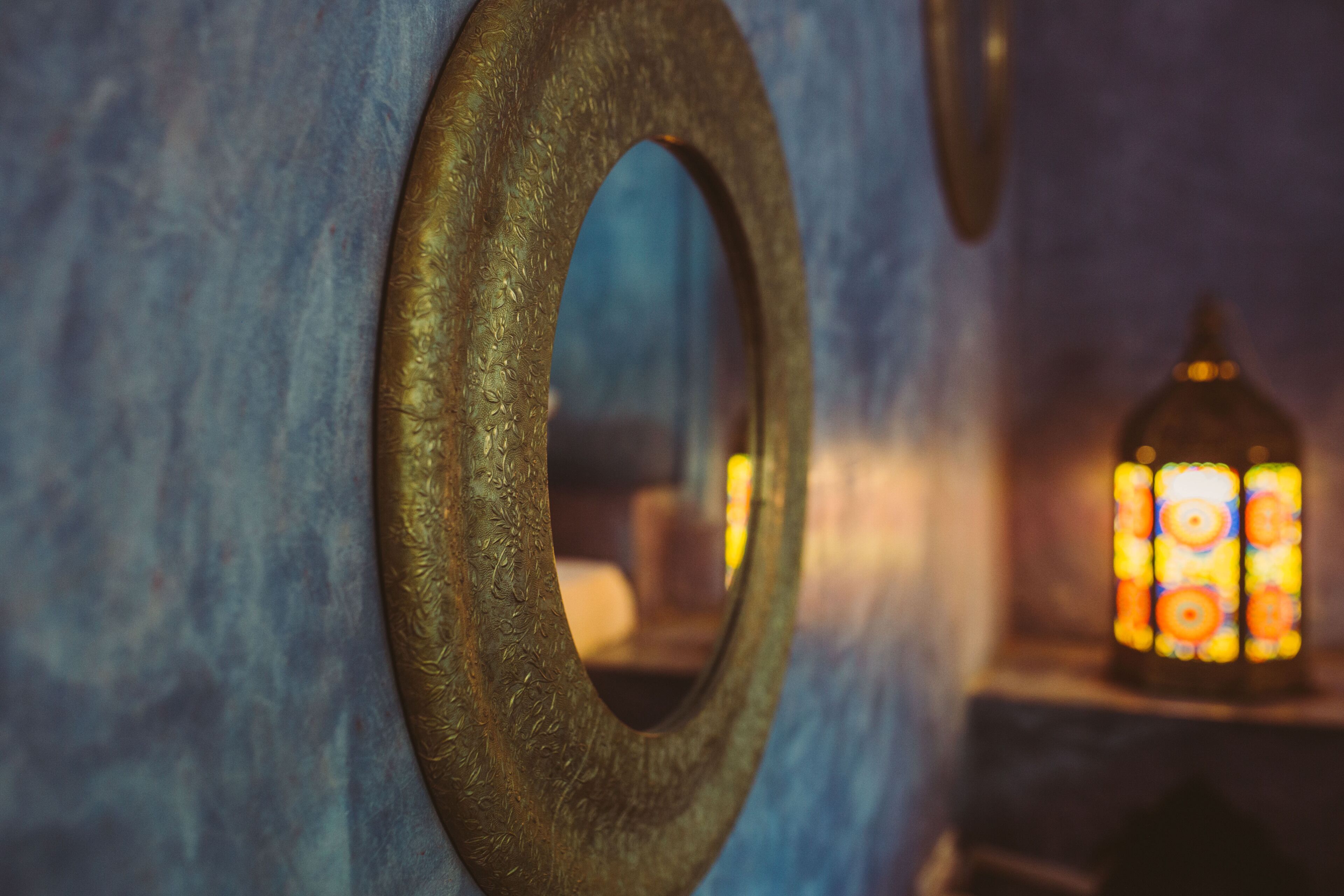 A close-up of a wall with a circular mirror and a stained glass window.