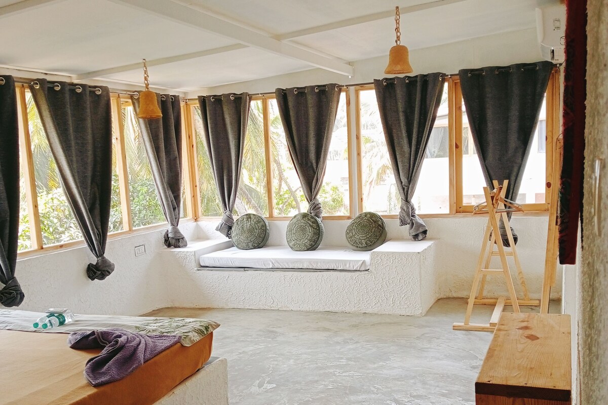 A room with a large window, a bed, a wooden bench, and a small table.