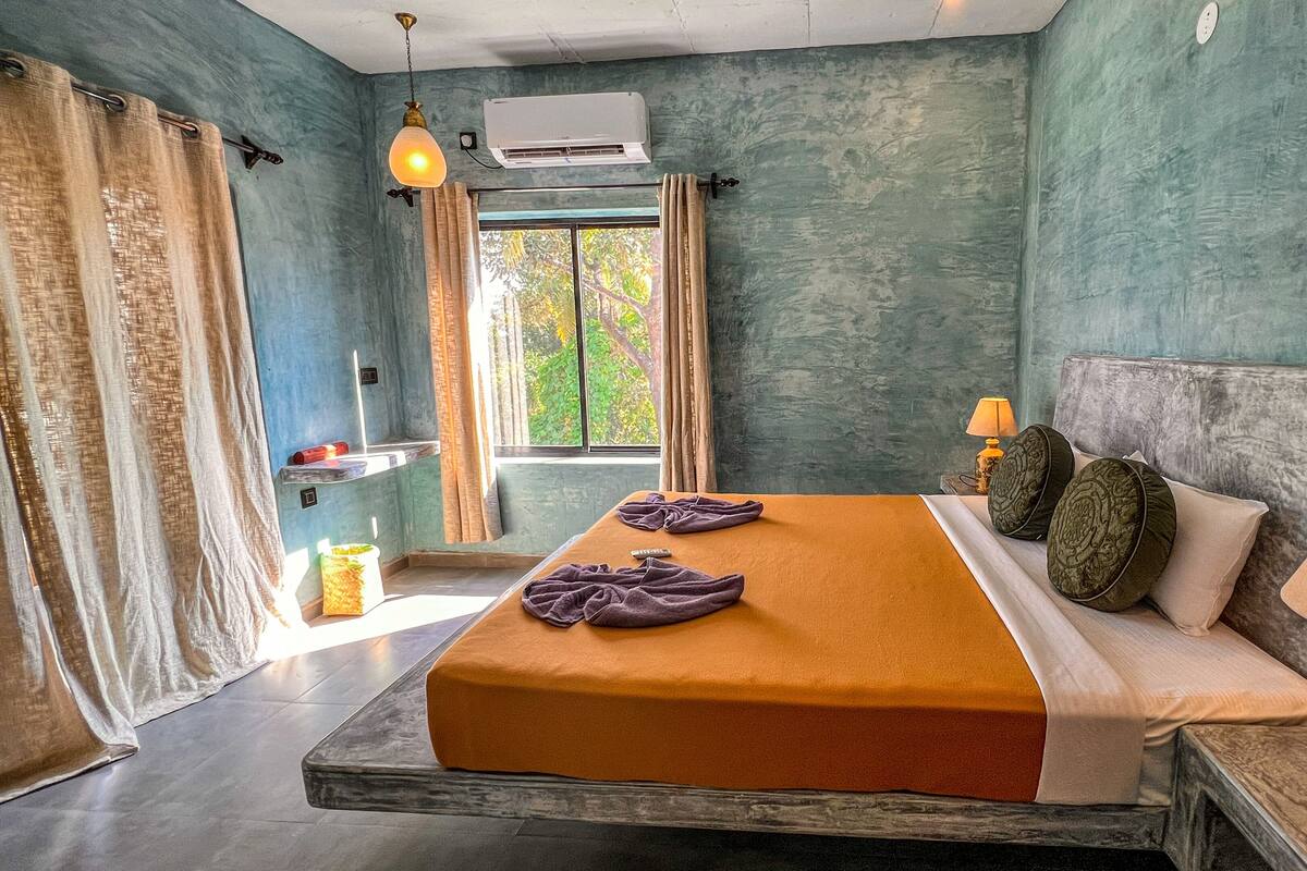 A bedroom with a bed, a nightstand, a lamp, a window, and curtains.